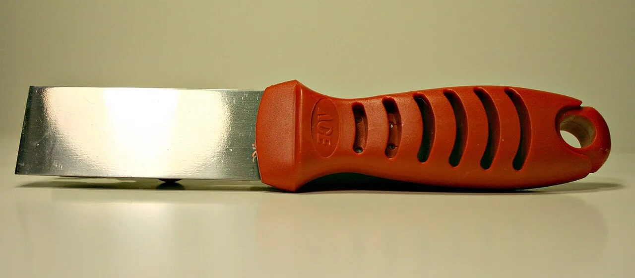 Putty knife blade used to lift cured adhesive from a floor